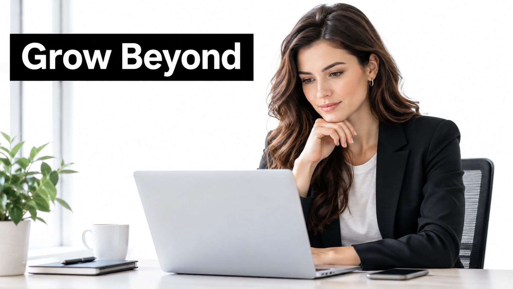A professional woman in a business suit working on a laptop at a bright, minimalist office desk.